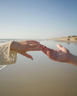 Two hands touching at a calm beach with clear sky and sandy shoreline in the background