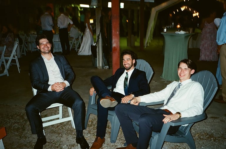Three men in business attire sitting on chairs at an outdoor evening event or gathering