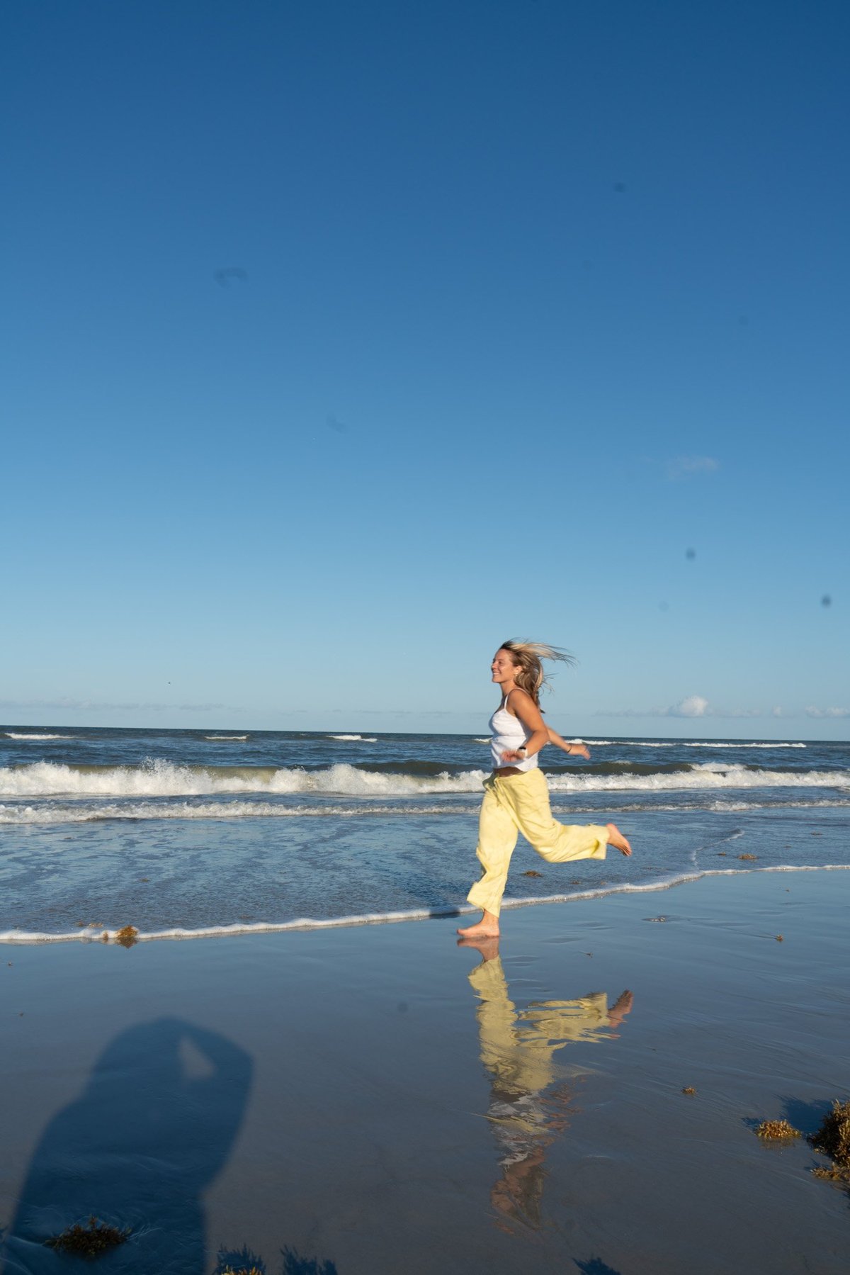 Woman jogging along wet sand beach with waves and clear blue sky in background