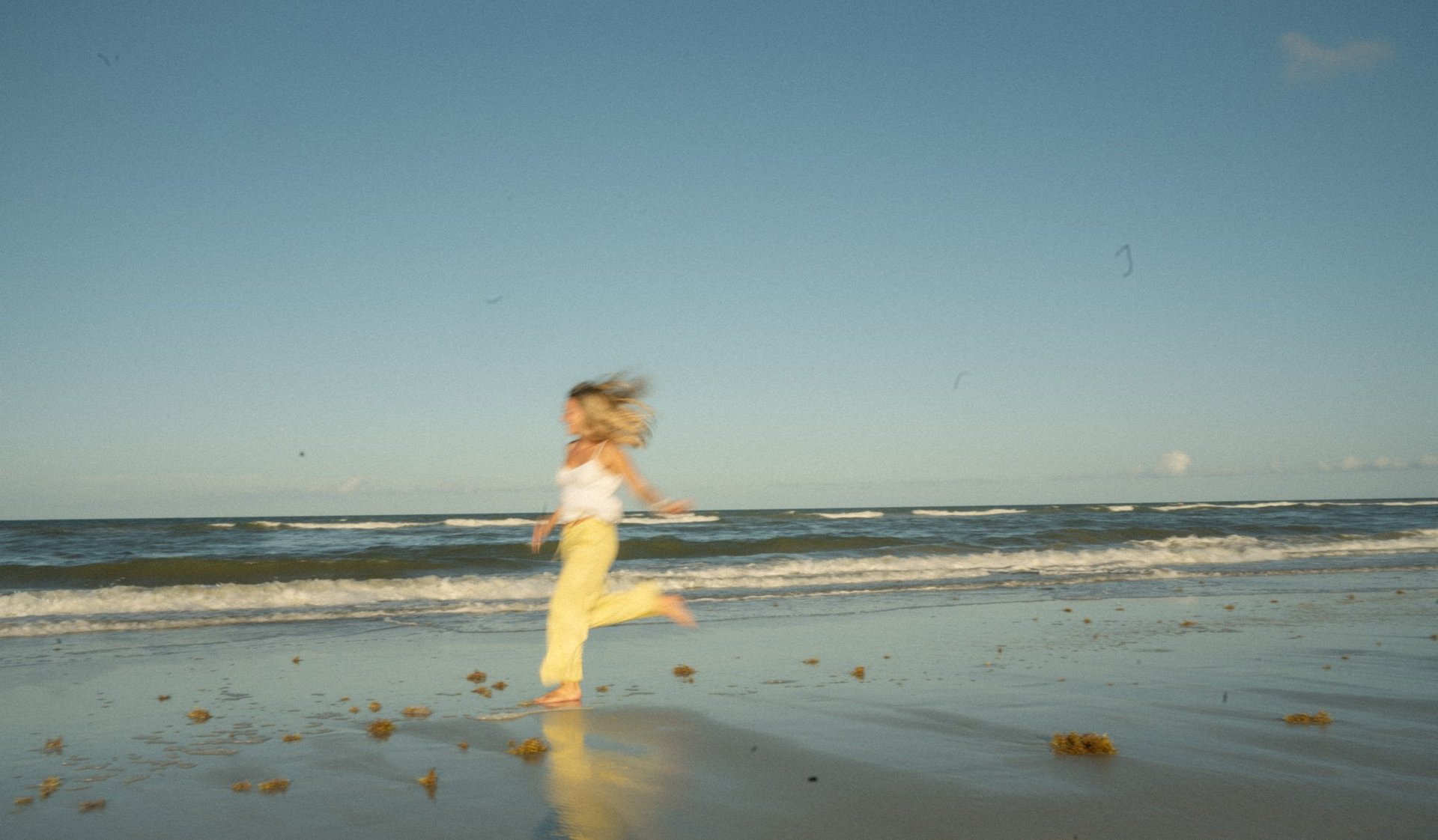 Woman in yellow dress running on wet beach with ocean waves in background