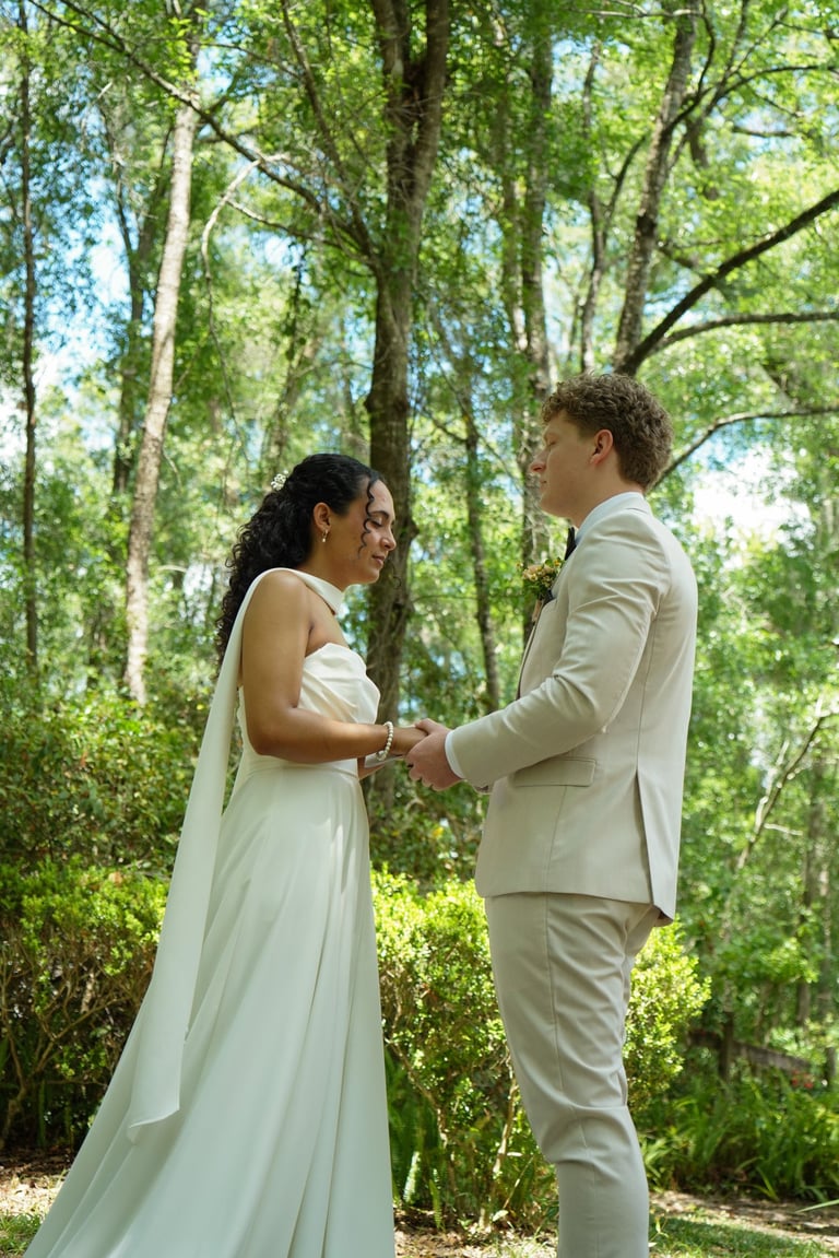 Bride and groom holding hands during outdoor wedding ceremony in a forest surrounded by tall green trees