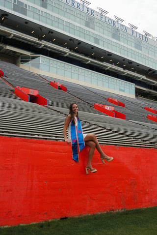 Woman in blue top posing on red stadium seating at Florida Field with striped upper stands visible
