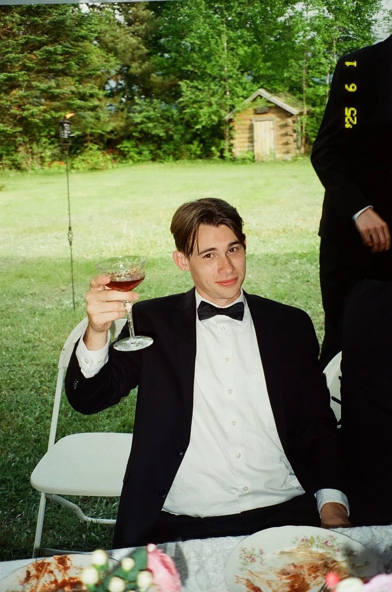 Man in black tuxedo and bow tie toasting with wine glass at outdoor garden event