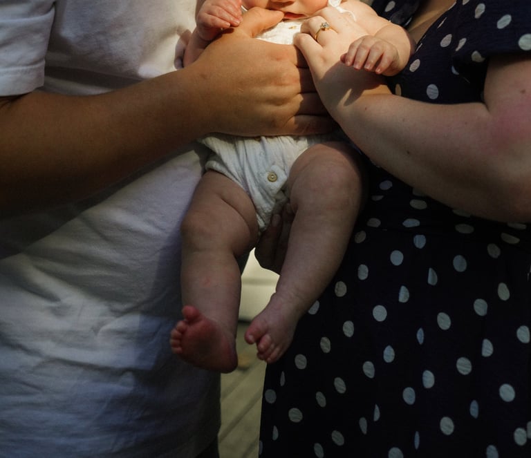 Two adults hold an infants legs and torso, displaying a bonding moment with the baby wearing a white diaper