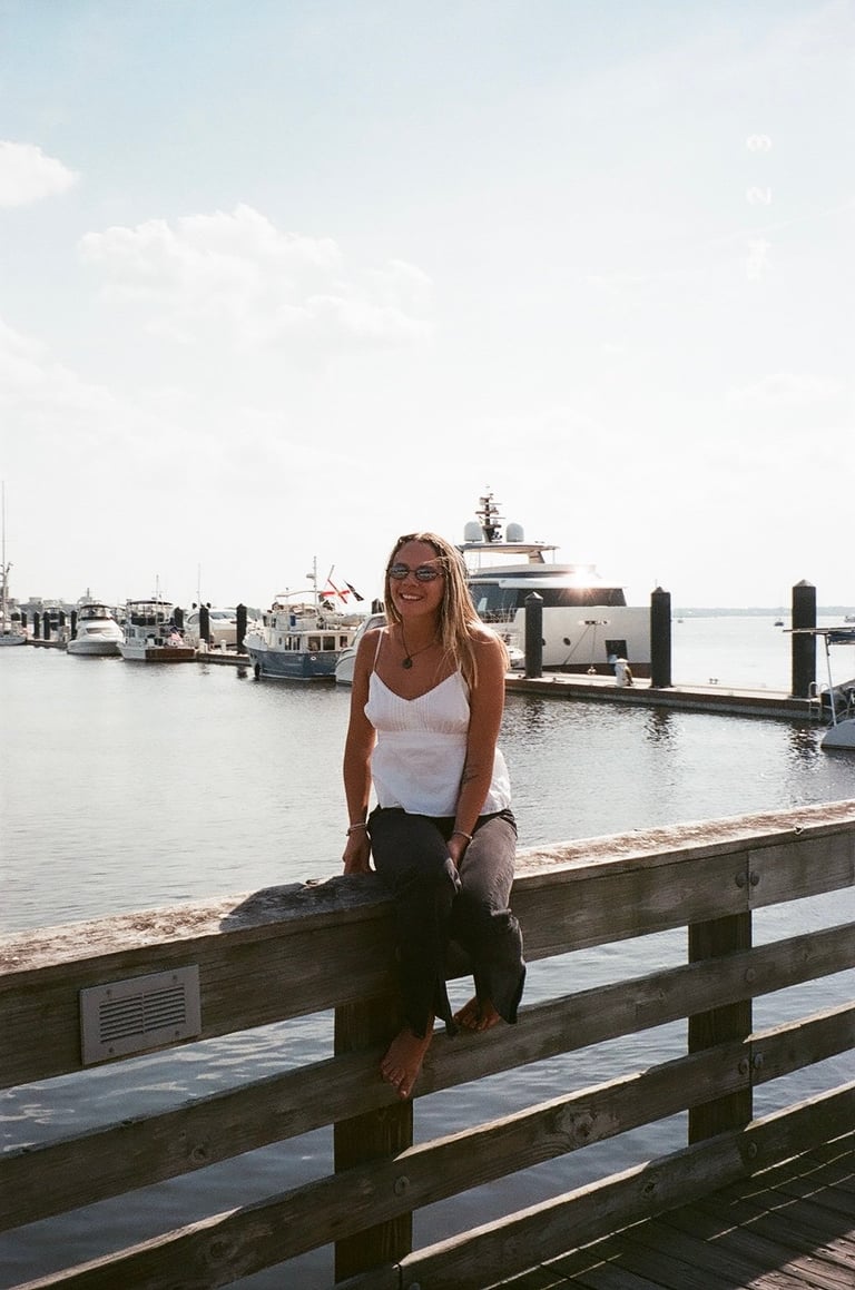 Woman sitting on wooden dock railing with boats and marina in background