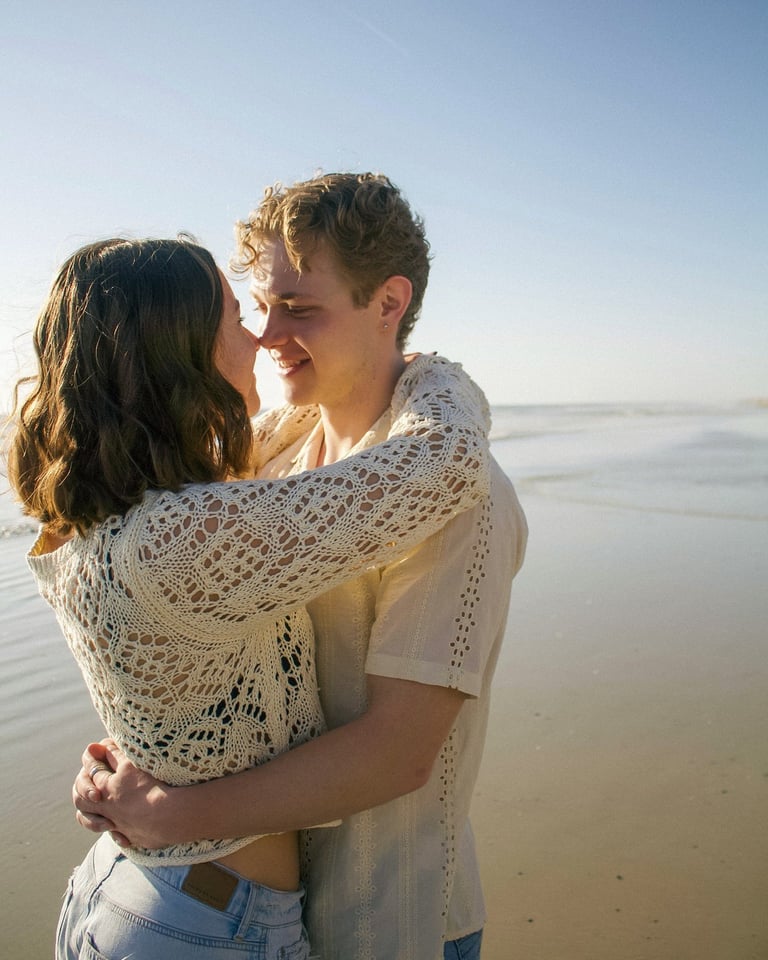 Couple embracing and smiling on a beach at sunset with calm water in background