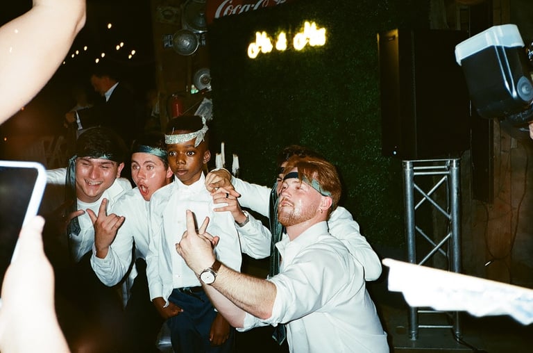 Four men in casual clothing posing playfully at a nightclub or bar with neon lights and green ivy wall backdrop