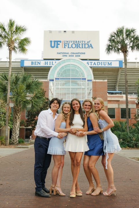 Five people in formal attire posing together in front of Ben Hill Stadium at University of Florida with palm trees visible
