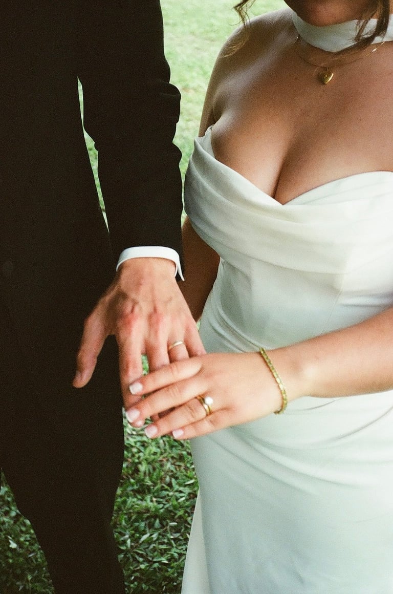 Bride and groom showing off wedding rings and hands together, bride in white dress and groom in black suit