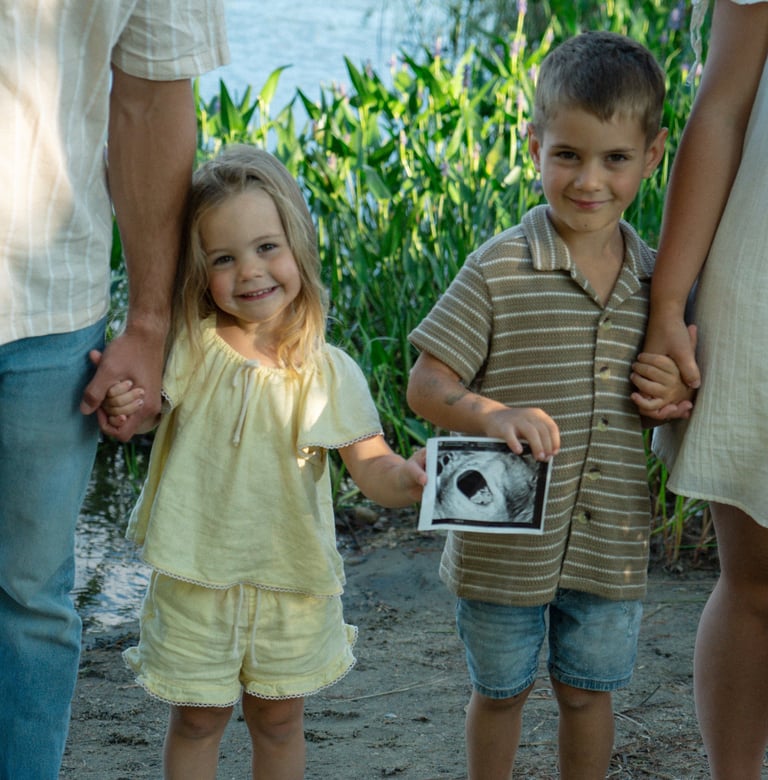 Two young children hold hands with adults in a cornfield, displaying an ultrasound image together