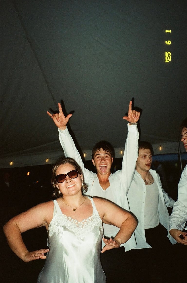Group of four people in white clothing celebrating indoors with raised arms and excited expressions