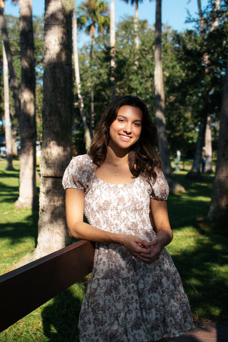 Woman in floral dress smiling in a park with tall palm trees and green grass on a sunny day