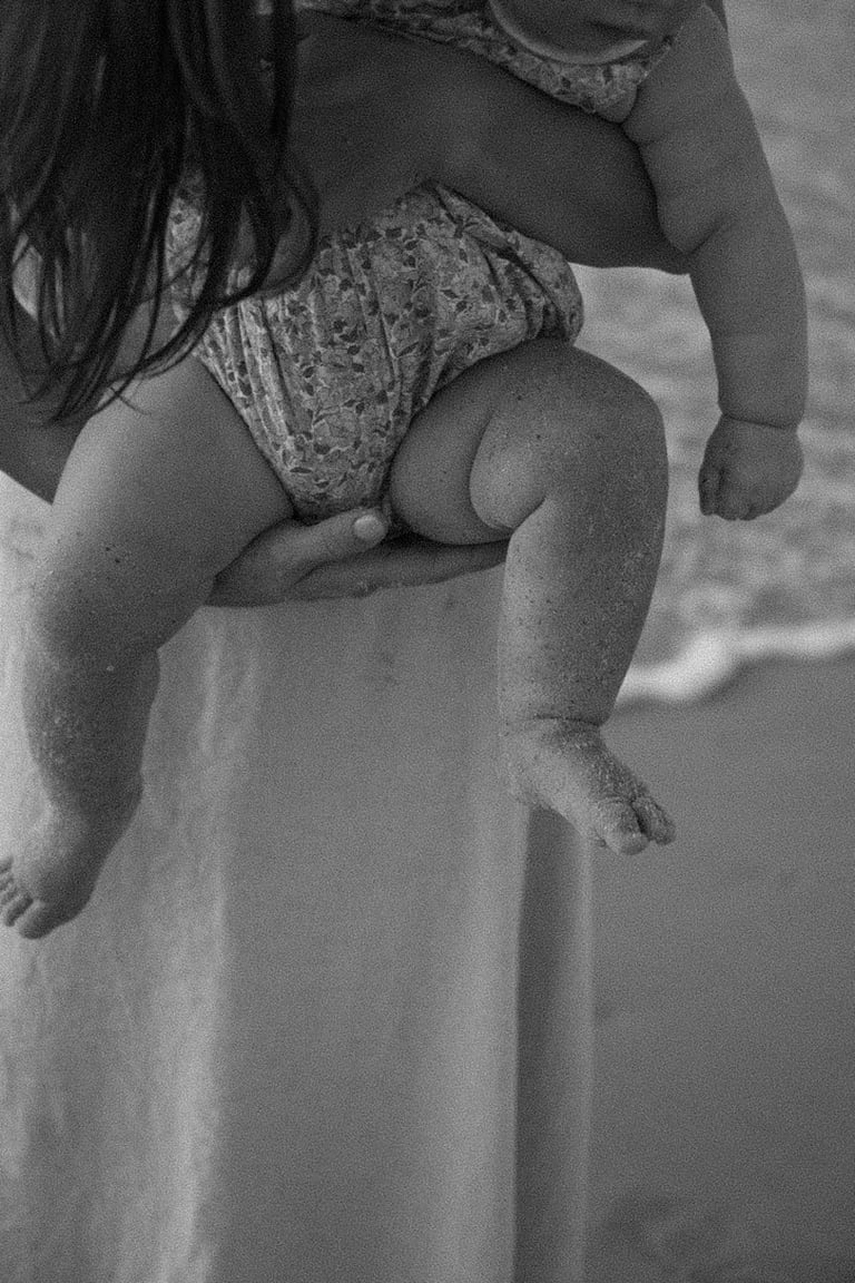 Adult holding a toddler on hip at the beach in black and white